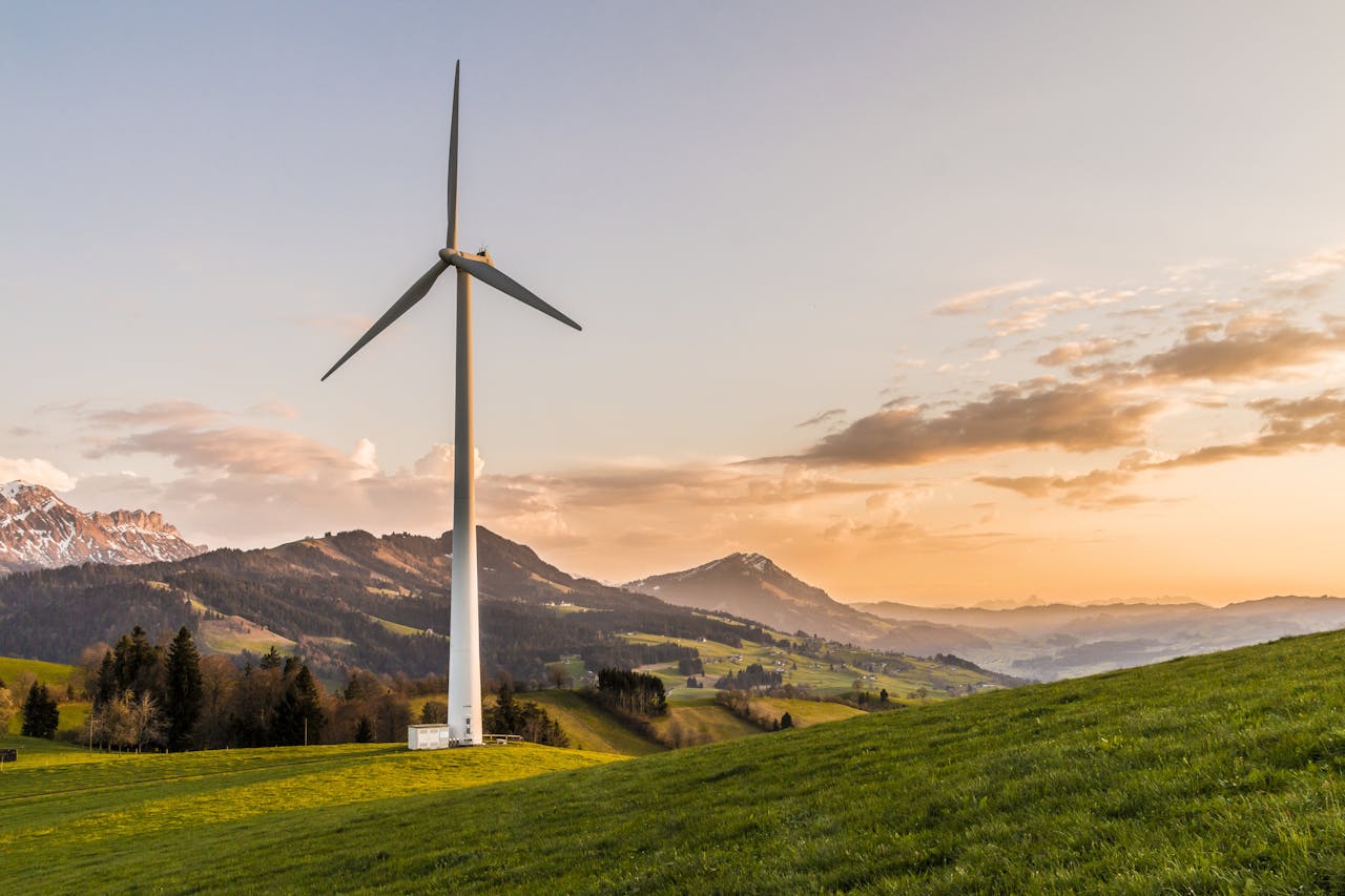 about-us Wind turbine amid rolling hills and mountains at sunset, symbolizing renewable energy and sustainability.